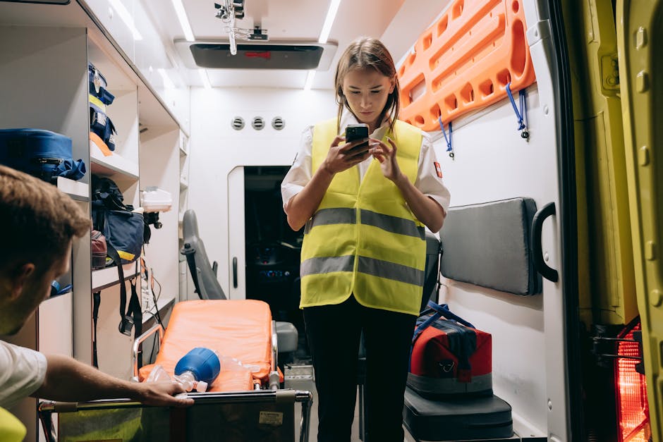Female paramedic using smartphone inside an ambulance preparing for emergency response.